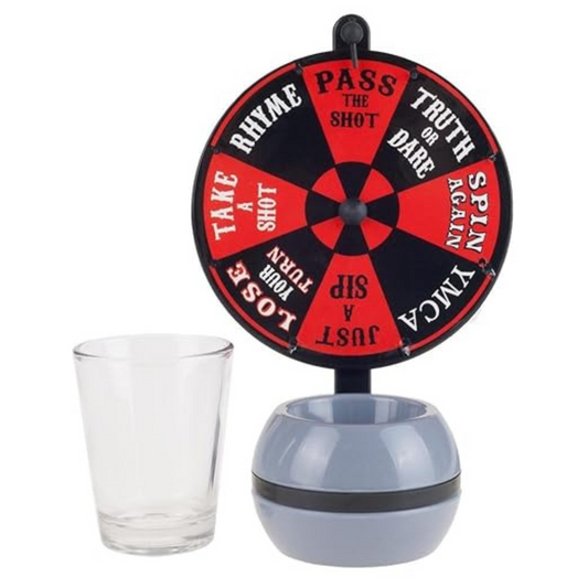 A drinking game set featuring a wheel with various drinking challenges written on it, such as 'PASS', 'RAHME', 'SHOT', 'DALE', 'TRUTH', 'DARE', 'LOST', 'TOAST', and 'DRINK AGAIN'. The wheel is mounted on a stand and there is a shot glass in front of it.