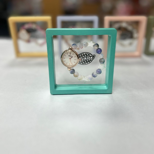 An analog watch with a gold casing and a multicolored beaded bracelet, displayed in a square-shaped frame.